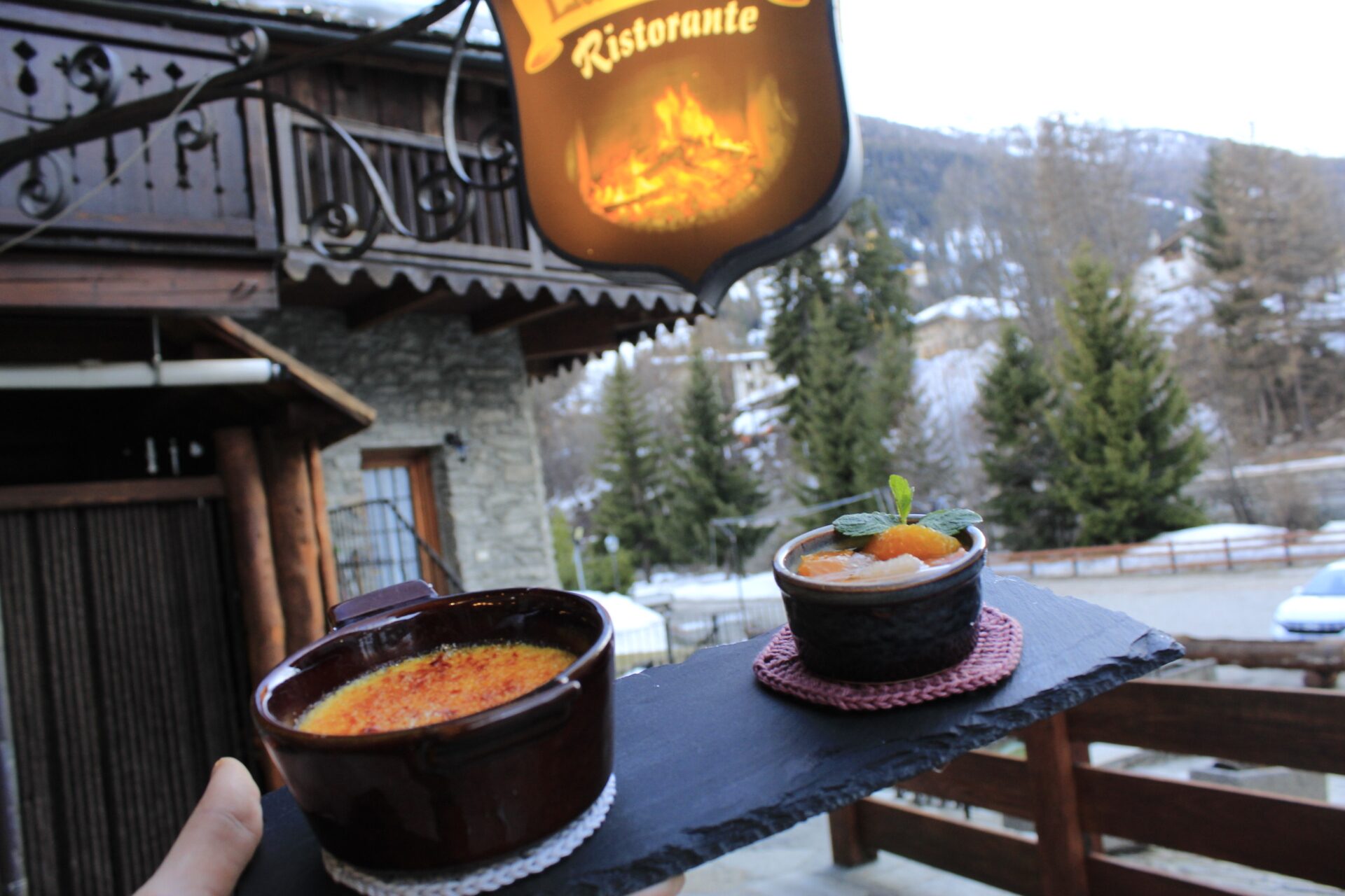 Dessert servito davanti all'insegna del Ristorante La Fordze con le montagne innevate di La Thuile sullo sfondo